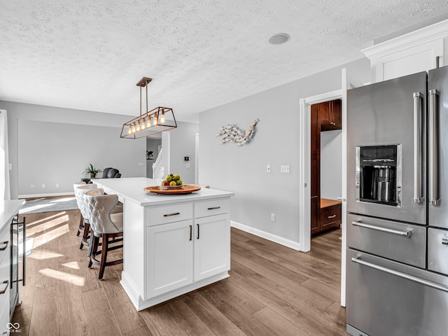 kitchen featuring light countertops, a kitchen breakfast bar, wood finished floors, high end fridge, and white cabinetry