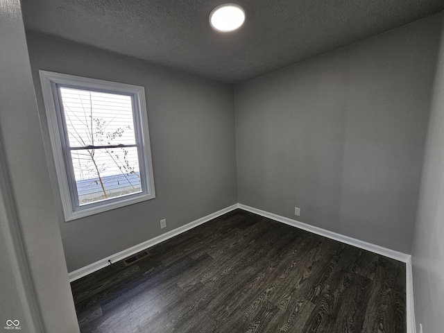 spare room featuring visible vents, baseboards, a textured ceiling, and dark wood-style floors