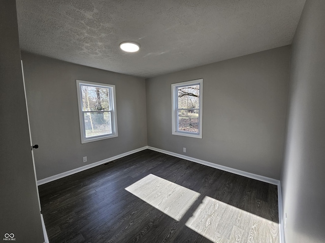 empty room with visible vents, baseboards, a textured ceiling, and dark wood-style floors