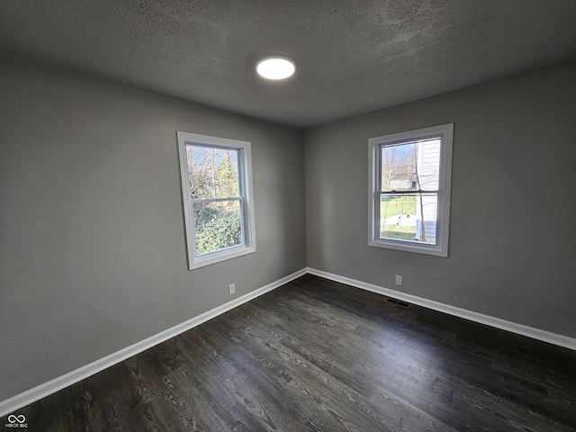 unfurnished room with visible vents, a healthy amount of sunlight, baseboards, and dark wood-style flooring