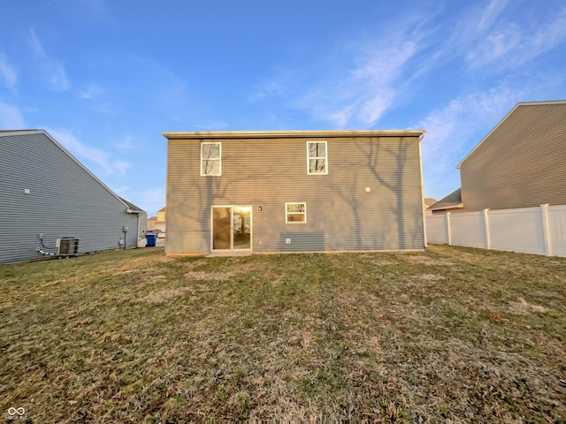 rear view of house with central air condition unit, a lawn, and fence