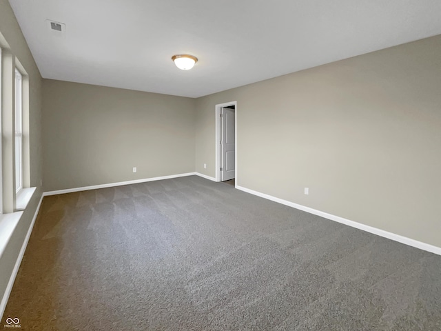 empty room featuring visible vents, baseboards, and dark colored carpet