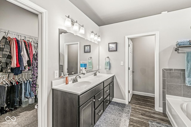 bathroom featuring a walk in closet, double vanity, a tub to relax in, and a sink