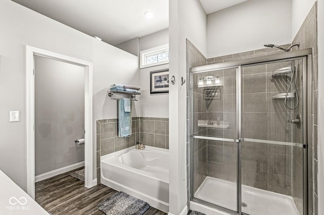 full bath with baseboards, wood finished floors, a stall shower, and a bath