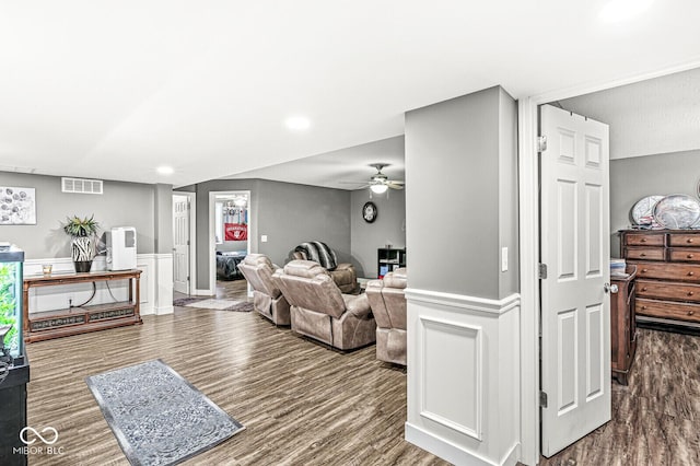 living room featuring a wainscoted wall, wood finished floors, visible vents, and ceiling fan