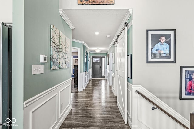 hall with crown molding, a decorative wall, a barn door, and dark wood-style flooring