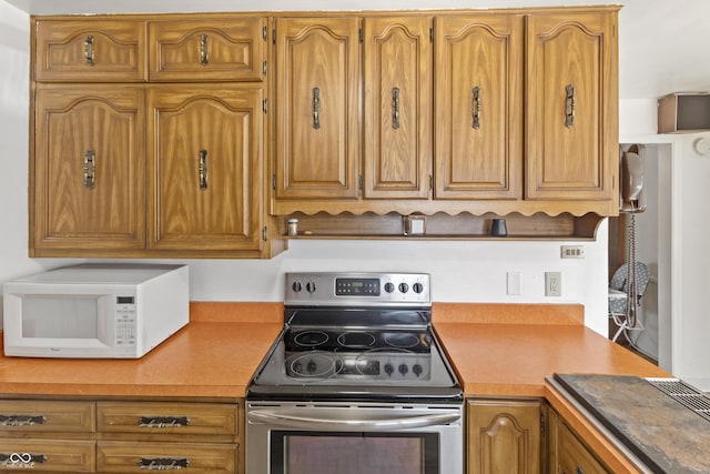 kitchen featuring white microwave, stainless steel range with electric stovetop, brown cabinetry, and light countertops