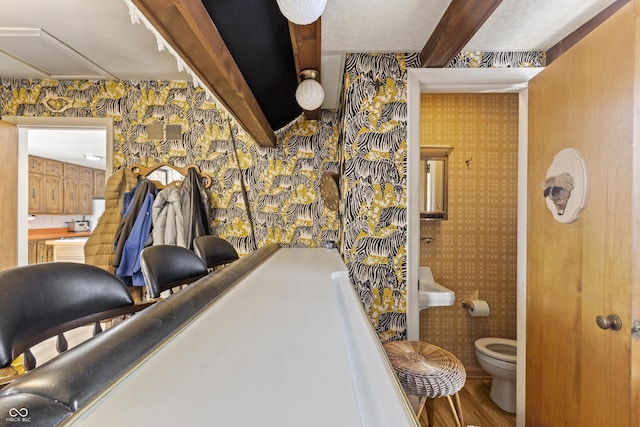 interior space featuring wallpapered walls, beam ceiling, and ensuite bathroom