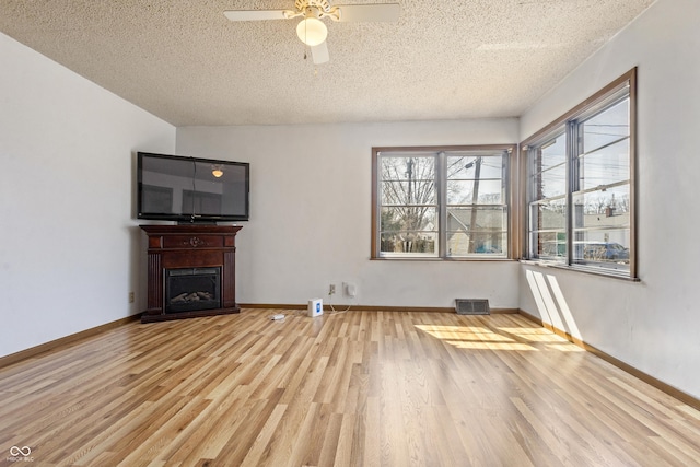 unfurnished living room with visible vents, baseboards, wood finished floors, a textured ceiling, and a ceiling fan