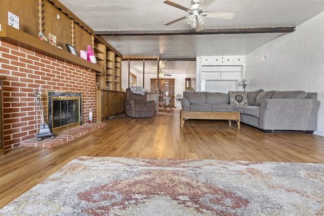 living area with beamed ceiling, a fireplace, ceiling fan, and wood finished floors