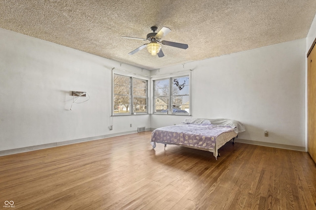 bedroom featuring visible vents, baseboards, wood finished floors, a textured ceiling, and a ceiling fan