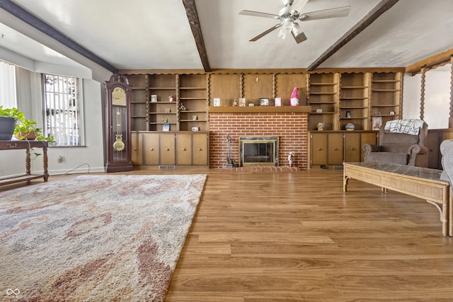 living area with beam ceiling, light wood-style flooring, baseboards, a brick fireplace, and ceiling fan