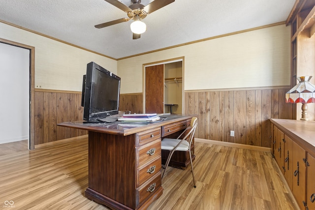 office area featuring a ceiling fan, a wainscoted wall, light wood finished floors, ornamental molding, and a textured ceiling