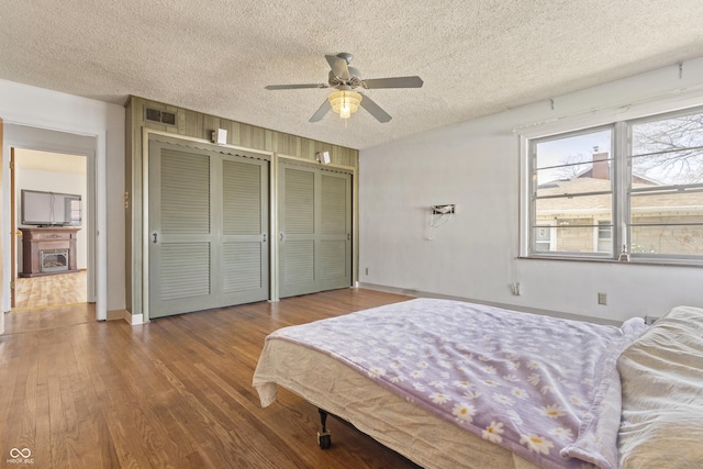 bedroom featuring visible vents, a textured ceiling, two closets, and wood finished floors