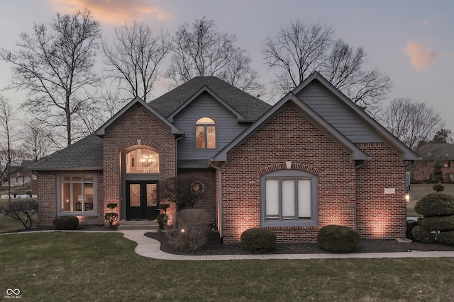 view of front of house with a front yard, brick siding, and roof with shingles