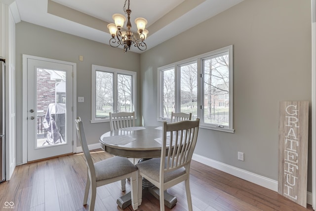 dining room with baseboards, a raised ceiling, a notable chandelier, and wood finished floors