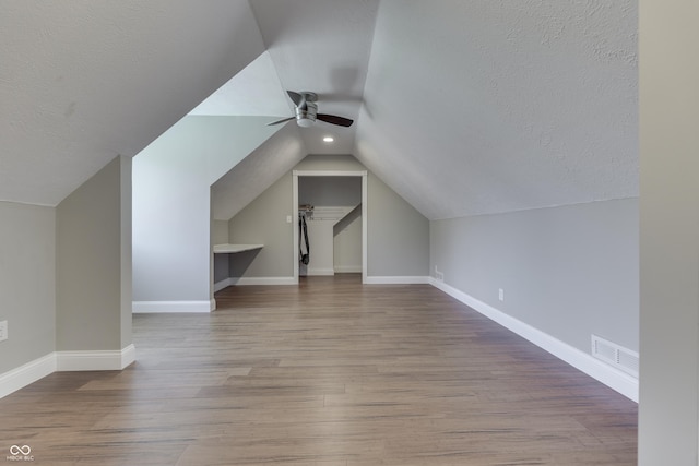 additional living space featuring baseboards, a textured ceiling, wood finished floors, and a ceiling fan