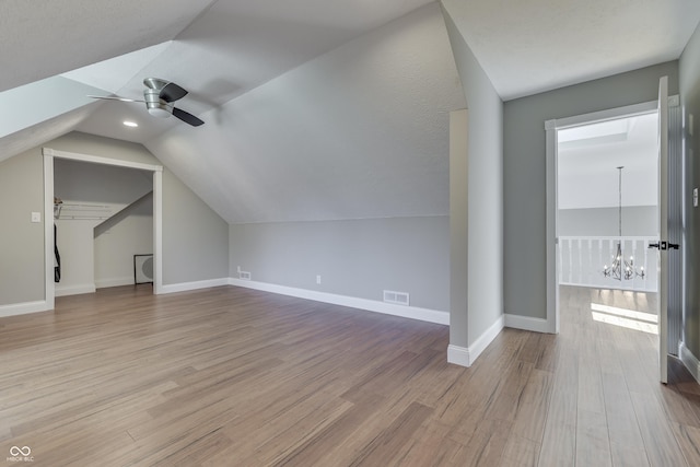 additional living space with visible vents, baseboards, wood finished floors, and ceiling fan with notable chandelier