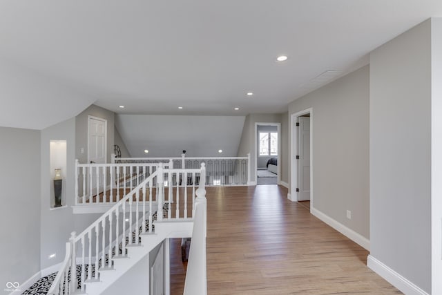 hall with an upstairs landing, lofted ceiling, recessed lighting, light wood-style floors, and baseboards