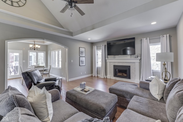 living room with wood finished floors, baseboards, arched walkways, a tile fireplace, and ceiling fan with notable chandelier