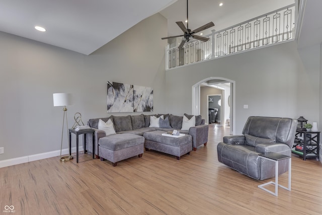 living area featuring a ceiling fan, baseboards, light wood finished floors, a high ceiling, and arched walkways