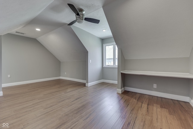 additional living space with lofted ceiling, a ceiling fan, a textured ceiling, wood finished floors, and baseboards