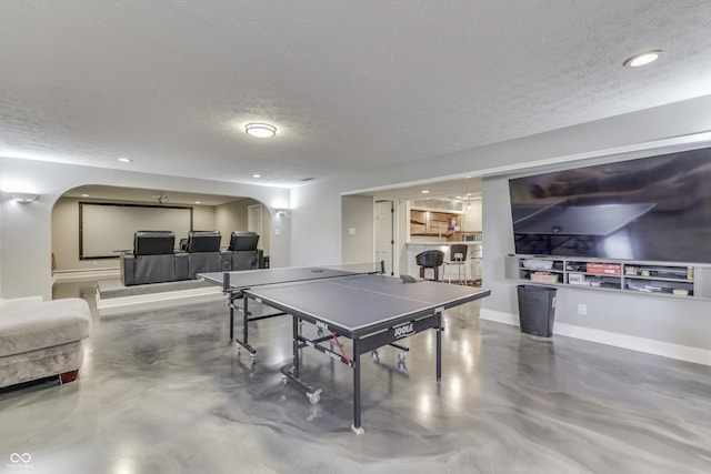 recreation room with baseboards, arched walkways, concrete flooring, and a textured ceiling