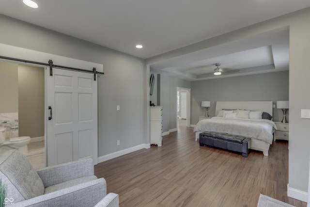 bedroom with a barn door, a raised ceiling, baseboards, and wood finished floors