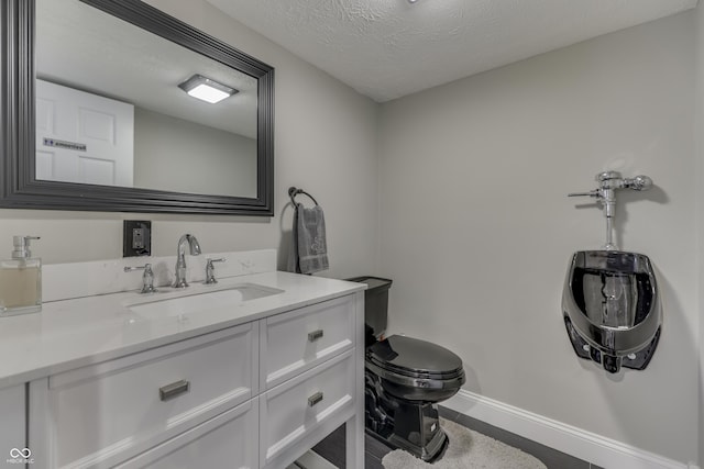 bathroom featuring toilet, a textured ceiling, vanity, and baseboards