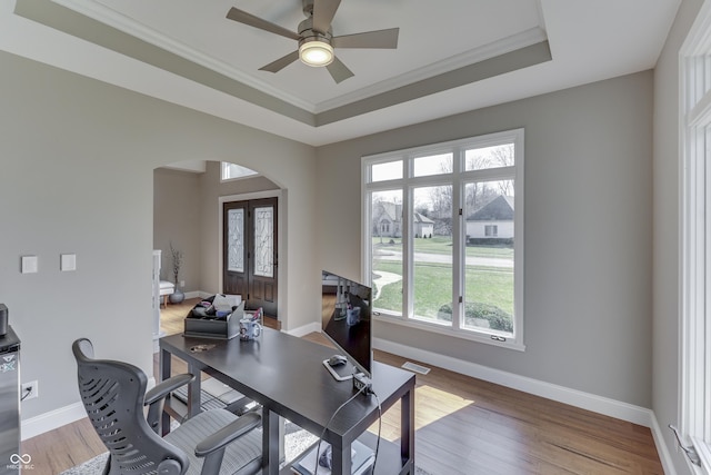 office area featuring arched walkways, a raised ceiling, wood finished floors, and crown molding