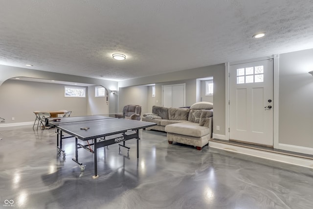 recreation room featuring baseboards, a textured ceiling, and concrete floors