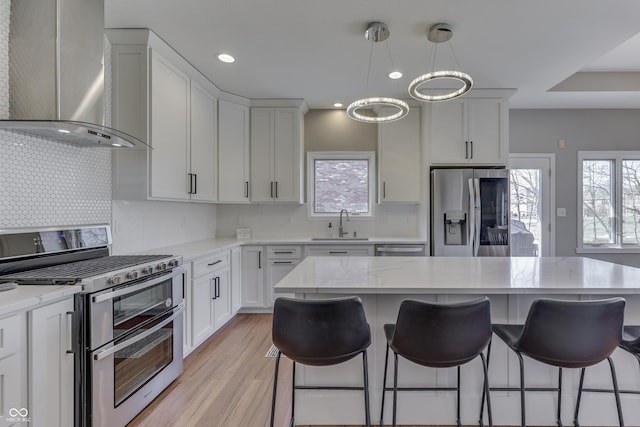 kitchen with wall chimney range hood, a breakfast bar area, appliances with stainless steel finishes, white cabinetry, and a sink