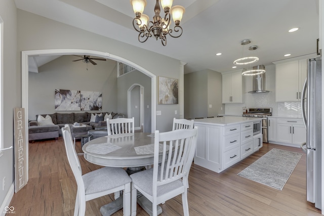 dining area featuring vaulted ceiling, recessed lighting, light wood-style flooring, ceiling fan with notable chandelier, and arched walkways