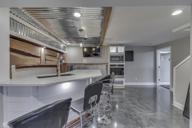 kitchen with baseboards, concrete floors, a sink, appliances with stainless steel finishes, and a kitchen breakfast bar