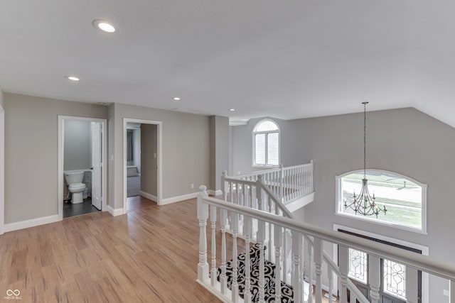 hallway with baseboards, light wood-type flooring, an upstairs landing, recessed lighting, and an inviting chandelier