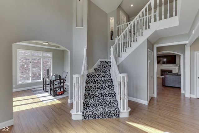 stairs featuring baseboards, a fireplace, a towering ceiling, wood finished floors, and arched walkways