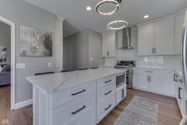 kitchen with light stone countertops, decorative backsplash, appliances with stainless steel finishes, wood finished floors, and wall chimney exhaust hood