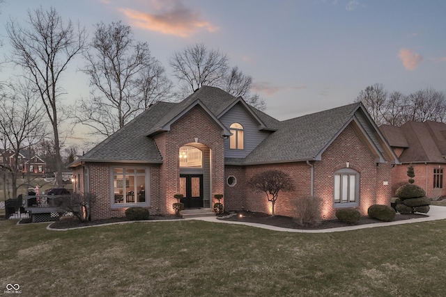 view of front of house with brick siding, a shingled roof, and a front lawn