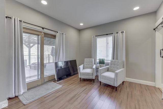 living area featuring a barn door, recessed lighting, baseboards, and wood finished floors