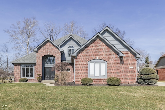 traditional-style house with brick siding, a front lawn, and a shingled roof