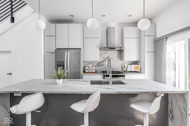 kitchen featuring a kitchen bar, wall chimney range hood, modern cabinets, and stainless steel fridge