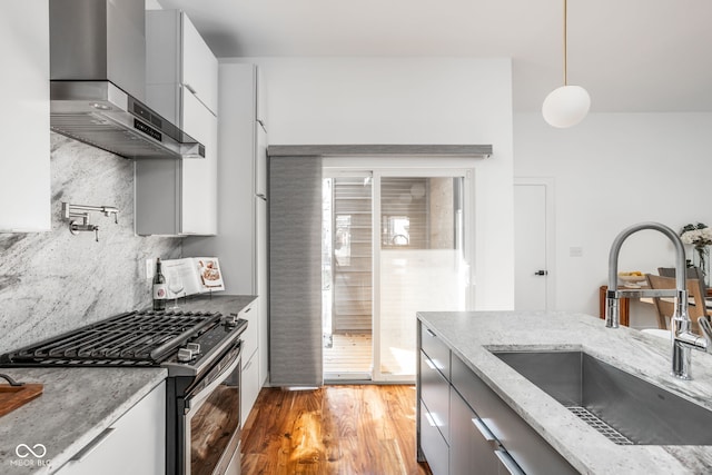 kitchen featuring a sink, gas range, wall chimney exhaust hood, modern cabinets, and light wood-type flooring