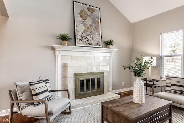 living area featuring a tile fireplace, baseboards, and vaulted ceiling