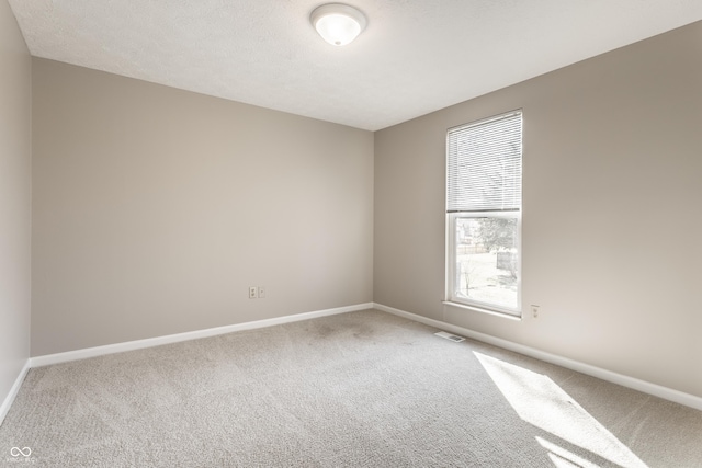 spare room featuring carpet flooring, baseboards, visible vents, and a textured ceiling