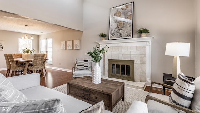 living area featuring a chandelier, a tiled fireplace, baseboards, and wood finished floors