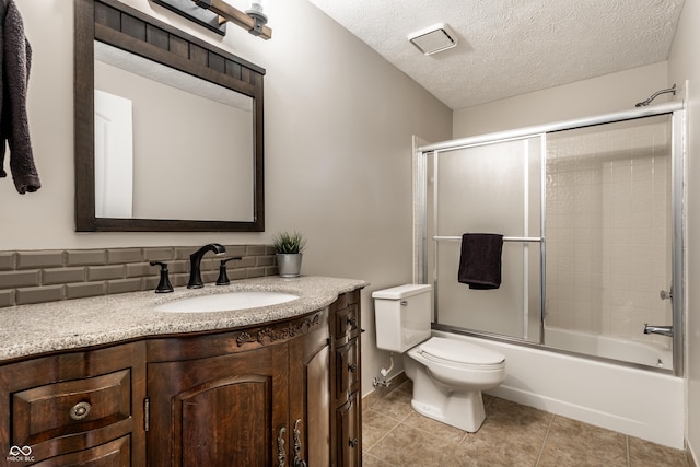 bathroom with tile patterned floors, toilet, a textured ceiling, combined bath / shower with glass door, and vanity