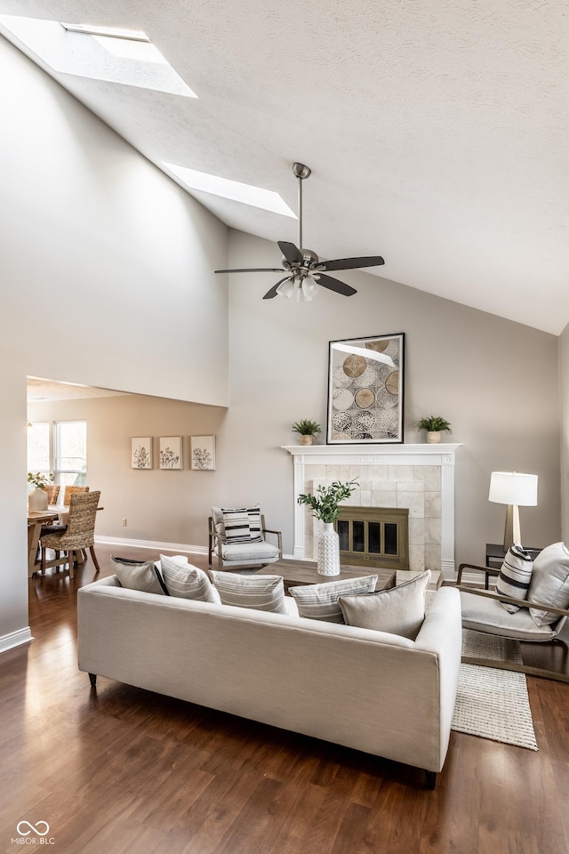 living area featuring wood finished floors, a skylight, a fireplace, baseboards, and ceiling fan