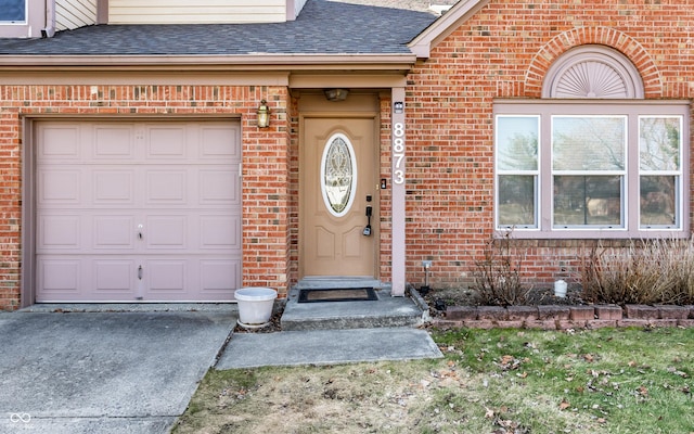 view of exterior entry featuring brick siding, driveway, and a shingled roof