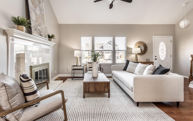 living area featuring ceiling fan, baseboards, lofted ceiling, a tile fireplace, and wood finished floors