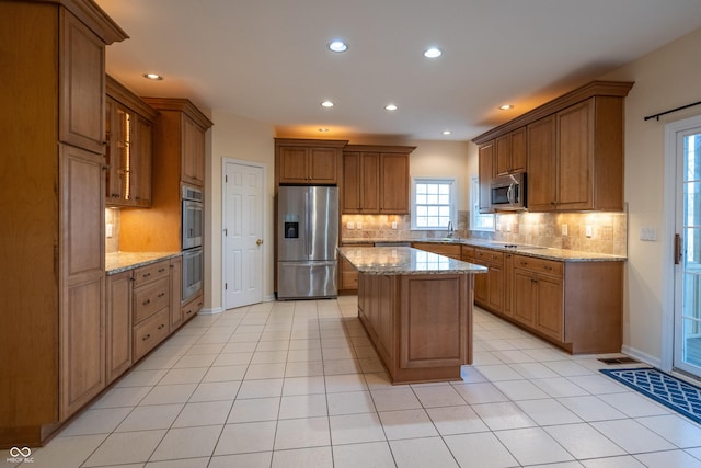 kitchen with light tile patterned floors, appliances with stainless steel finishes, a kitchen island, and light stone countertops